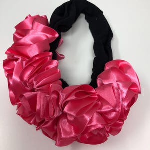 May include: A black stretchy headband with a large pink satin bow. The bow is made of multiple layers of ribbon and is very full.