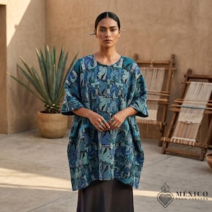 May include: A loose-fitting, short-sleeved tunic featuring a complex, multi-tonal blue and teal geometric pattern. The garment has a wide, boxy silhouette and is paired with a solid dark-colored skirt. A silver hair accessory is visible.