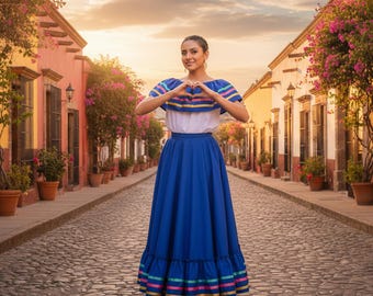 May include: A woman in a traditional Mexican dress stands on a cobblestone street. The dress features a white top with blue and yellow stripes, a long blue skirt, and colorful trim. The image is set against a backdrop of colorful buildings and a sunset.