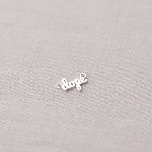 May include: Silver charm with the word "dope" written in a cursive font.