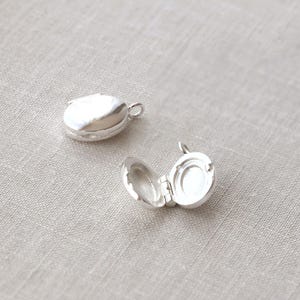 May include: Two silver locket pendants, one closed and one open, showing the inside of the locket. The locket is oval shaped with a hinged lid.