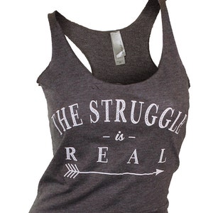 May include: A dark gray tank top with a white graphic that reads "THE STRUGGLE is REAL" with an arrow pointing to the right.