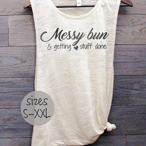 Pode incluir: Um top branco sem mangas com o texto "Messy bun & getting stuff done" em preto. O top tem uma parte inferior amarrada e est&aacute; dispon&iacute;vel nos tamanhos S-XXL.