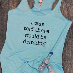May include: A light blue tank top with the text "I was told there would be drinking." printed on the front. Two bottles of vodka are lying on the tank top.