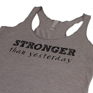 May include: Gray tank top with the text "STRONGER than yesterday" printed in black.