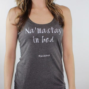 Puede incluir: Un top de tirantes gris oscuro con el texto "Na'maste in bed" y el hashtag "#savasana" en blanco.