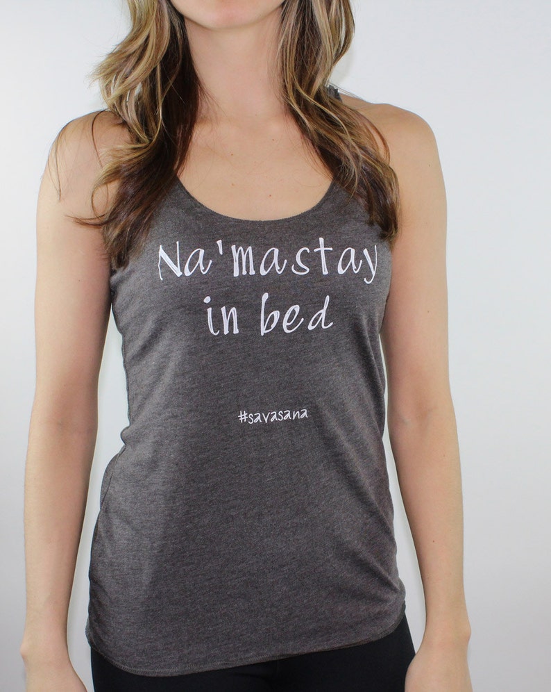 Puede incluir: Un top de tirantes gris oscuro con el texto "Na'maste in bed" y el hashtag "#savasana" en blanco.