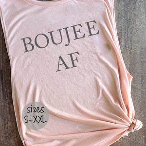 May include: A light pink sleeveless tank top with the text "BOUJEE AF" printed in gray. The tank top has a round label with the text "sizes S-XXL" printed in black.