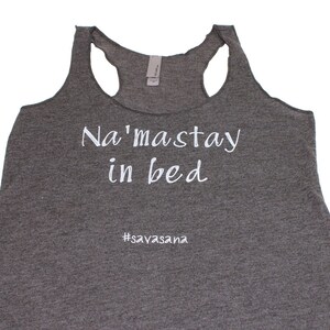 Puede incluir: Camiseta de tirantes gris con el texto "Na'masstay in bed #savasana" impreso en blanco.