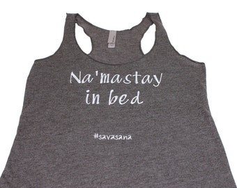 Può includere: Canotta grigia con la scritta "Na'masstay in bed #savasana" stampata in bianco.