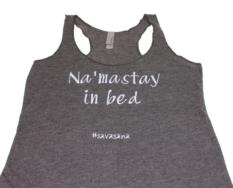 Puede incluir: Camiseta de tirantes gris con el texto "Na'masstay in bed #savasana" impreso en blanco.