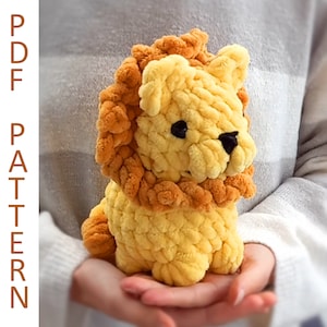 May include: A crocheted lion plush toy with a yellow body and orange mane. The lion is sitting on a person's hands.