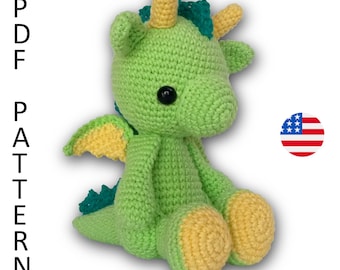 Puede incluir: Juguete de amigurumi de dragón verde tejido a crochet con detalles amarillos y verde azulado. El dragón tiene un cuerno amarillo, patas amarillas y alas verde azuladas. El juguete está sentado sobre un fondo blanco.