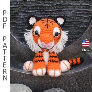 May include: A crocheted tiger amigurumi toy with orange and black stripes, white fur, and black eyes. The toy is sitting on a grey stone surface.