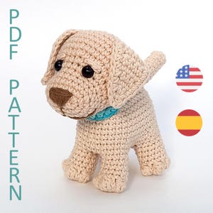 Könnte beinhalten: Ein gehäkeltes cremefarbenes Labrador-Welpe mit brauner Nase und schwarzen Augen. Der Welpe trägt ein hellblaues Halsband. Das Bild enthält den Text "PDF PATTERN" in Türkis.