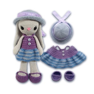 May include: A crocheted bunny doll wearing a purple and blue dress, a matching hat, and shoes. The doll has a grey body and a pink nose.