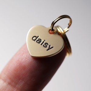 Puede incluir: Chapa de identificación para mascotas en forma de corazón de oro con el nombre "daisy" grabado en letras negras.