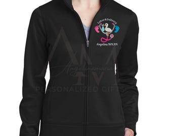 May include: Black zip-up jacket with a white embroidered design of a stethoscope, a stork, and two baby footprints. The text "Labor & Delivery" and "Angelina BSN, RN" is also embroidered on the jacket.