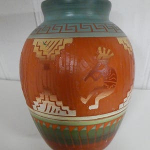 Peut inclure: Un vase en céramique peint à la main avec un motif du Sud-Ouest. Le vase est orange avec des accents blancs et verts. Il présente une figure stylisée au centre.