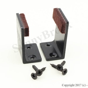 May include: Two black metal brackets with brown felt pads on the bottom. The brackets are designed to be mounted to a wall. Three black screws are included.