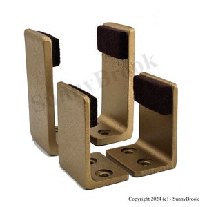 May include: Four gold metal wall mounted hooks with brown felt pads. The hooks are designed to hold items like coats, hats, or bags.