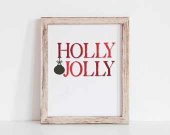 Może przedstawiać: Wydruk w ramie z tekstem "HOLLY JOLLY" w czerwonych literach. Mała zielona i czarna ozdoba wisi nad słowem "JOLLY".
