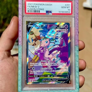 Może przedstawiać: Karta Pokémon z Mew z zestawu Fusion Strike, oceniona i chroniona w etui z fioletowymi i turkusowymi obramowaniami. Tekst na karcie zawiera "Energy Mix" i "Psychic Leap".