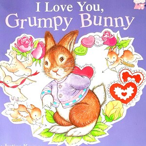 May include: A children's book titled "I Love You, Grumpy Bunny" with a purple cover. The cover features an illustration of a brown bunny wearing a purple jacket, surrounded by hearts, roses, and small birds. The book is by Justine Korman and illustrated by Lucinda McQueen.