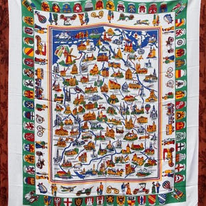 May include: White tablecloth featuring a detailed map with illustrations of landmarks, vehicles, and coats of arms. The map is bordered by a green and white design with additional illustrations. The tablecloth is rectangular.