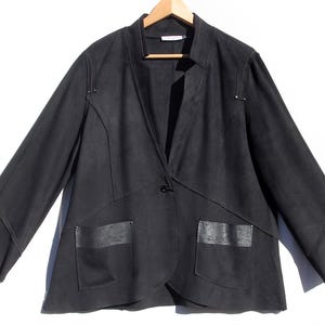 May include: A black blazer with a single button closure and two front pockets. The blazer has a unique design with angular seams and decorative stitching. The sleeves are long, and the jacket is hanging on a wooden hanger.