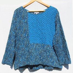May include: A long-sleeved top featuring a color-blocked design with a bright blue textured panel on the upper chest and a black and blue speckled pattern covering the remainder of the garment, including the sleeves and the lower body section.