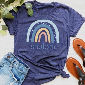 May include: A navy blue t-shirt with a rainbow design and the word "shalom" printed on it.