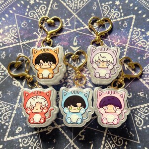 May include: A collection of six keychains featuring cartoon characters in cat costumes. Each keychain has a gold-colored heart-shaped clasp. The characters are in various colors, including orange, pink, red, blue, and purple.