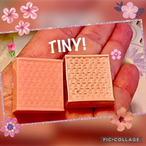 May include: Two small, square, peach-colored boxes are held in a hand. One box has a textured surface, while the other has a patterned design. The word "TINY!" is written above the boxes. The image has a floral border.
