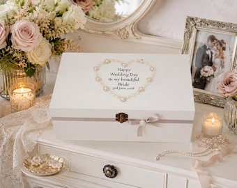 May include: A white rectangular wooden keepsake box featuring a heart-shaped border of pearls and rhinestones on the lid. The text reads: Happy Wedding Day to my beautiful Bride 3rd June 2018. The box has a metal latch and a grey ribbon with a small bow.