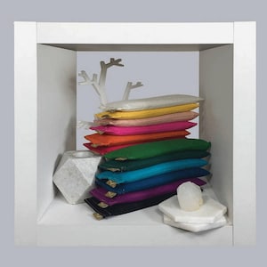 Puede incluir: Una pila de almohadas rectangulares coloridas en una vitrina blanca. Las almohadas son de varios colores, incluyendo amarillo, rosa, naranja, verde, azul y morado. Un &aacute;rbol decorativo blanco y un portavelas geom&eacute;trico tambi&eacute;n est&aacute;n presentes.