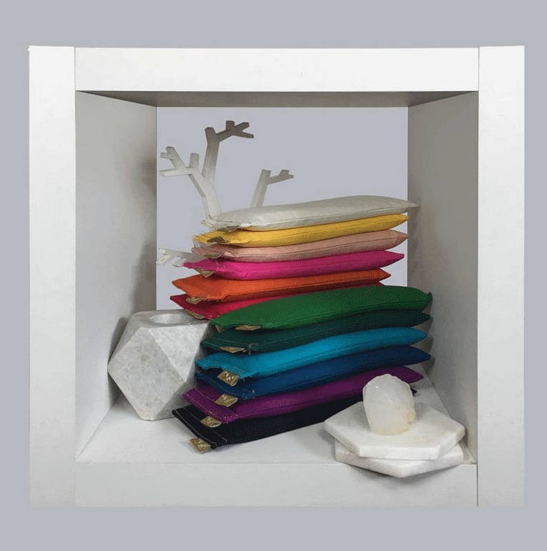 Puede incluir: Una pila de almohadas rectangulares coloridas en una vitrina blanca. Las almohadas son de varios colores, incluyendo amarillo, rosa, naranja, verde, azul y morado. Un &aacute;rbol decorativo blanco y un portavelas geom&eacute;trico tambi&eacute;n est&aacute;n presentes.