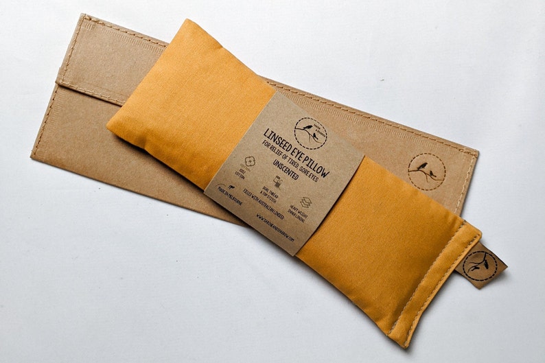 Puede incluir: Almohada para ojos de linaza de color mostaza con una funda de papel marr&oacute;n. La almohada lleva la etiqueta "Linseed Eye Pillow for Relief of Tired Sore Eyes Unscented". El embalaje incluye un peque&ntilde;o logotipo de p&aacute;jaro y detalles.