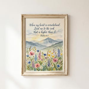 Op de afbeelding: Een ingelijste kunstdruk met een aquarellandschap van bergen onder een zachte lucht, met een veld vol kleurrijke wilde bloemen op de voorgrond. De tekst luidt: When my heart is overwhelmed; Lead me to the rock that is higher than I. Psalm 61:2.