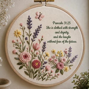 Peut inclure: Un tambour à broder circulaire en bois contenant un tissu blanc cassé avec des motifs floraux brodés à la main en rose, jaune et violet, incluant un petit papillon et le texte : Proverbs 31:25 She is clothed with strength and dignity, and she laughs without fear of the future.