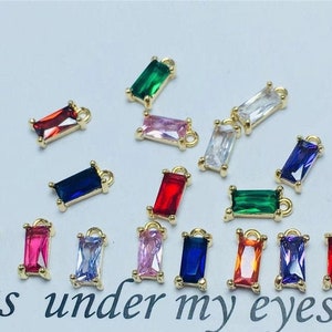 May include: Assortment of colorful rectangular shaped charms with gold settings. The charms feature various colors including red, blue, green, pink, and clear.
