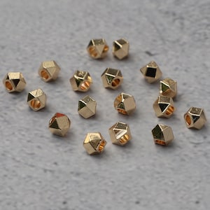 Può includere: Una collezione di 16 perline in metallo dorato con un design geometrico sfaccettato. Ogni perlina ha un foro al centro per essere infilata.