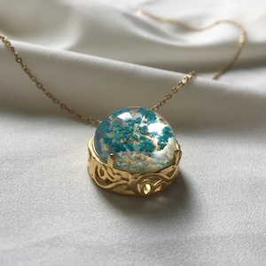 May include: A gold necklace with a round pendant featuring a teal flower encased in clear resin.