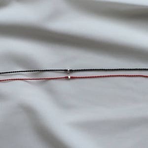 May include: Two bracelets, one black and one red, with silver beads on a white background.