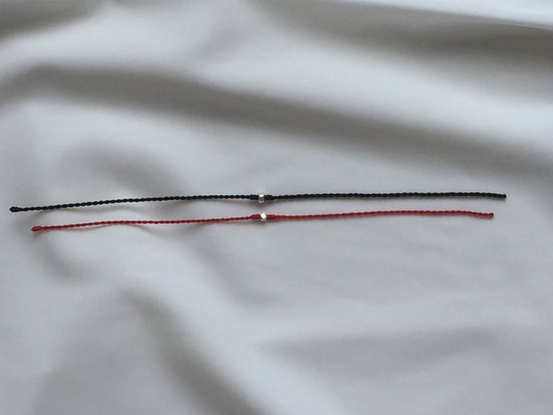 May include: Two bracelets, one black and one red, with silver beads on a white background.