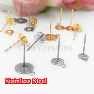 May include: A close-up of a selection of earring findings, including gold and silver-toned post earrings with loops. The findings are arranged on a white surface. The text "Stainless Steel" is visible in the bottom left corner of the image.