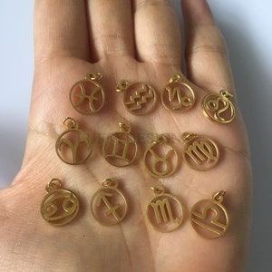 Pode incluir: Doze pingentes de metal dourado com os signos astrol&oacute;gicos do zod&iacute;aco. Os pingentes s&atilde;o redondos e t&ecirc;m um furo na parte superior para serem presos a um colar ou pulseira.