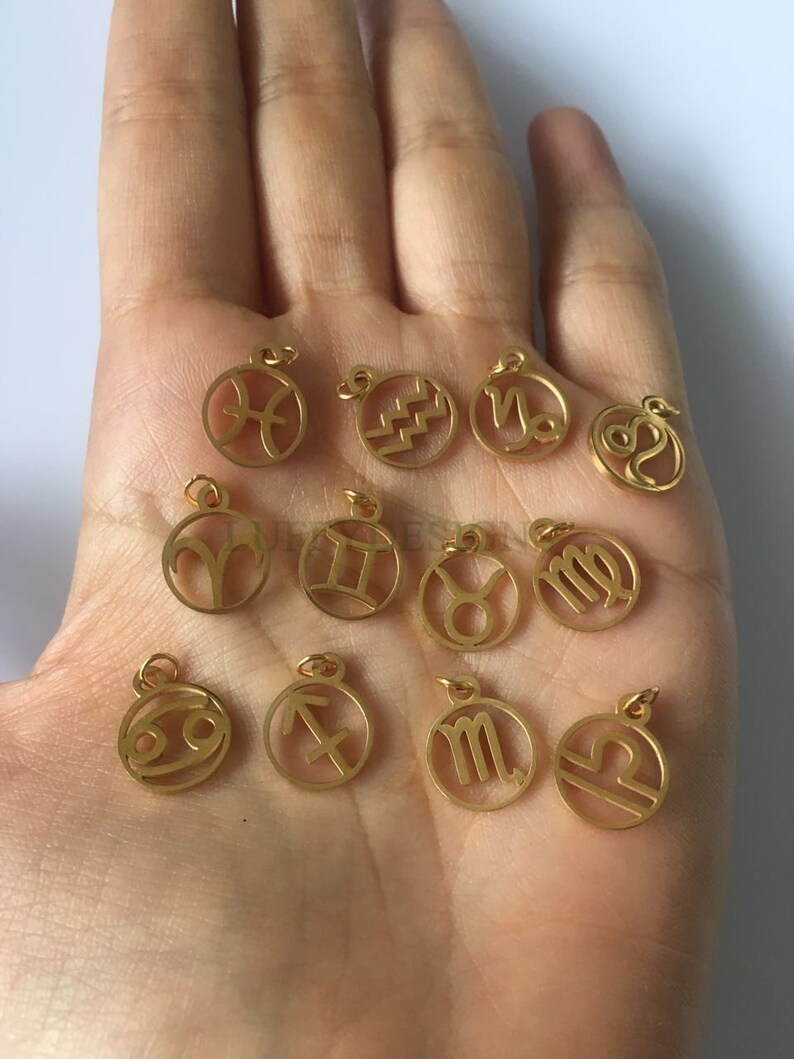 Pode incluir: Doze pingentes de metal dourado com os signos astrol&oacute;gicos do zod&iacute;aco. Os pingentes s&atilde;o redondos e t&ecirc;m um furo na parte superior para serem presos a um colar ou pulseira.