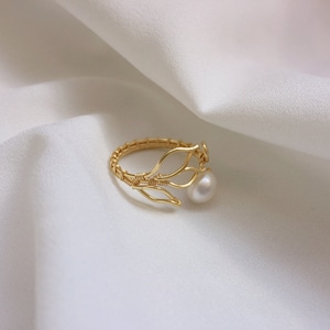 May include: A gold ring featuring a delicate wire design resembling branches, adorned with a single white pearl.