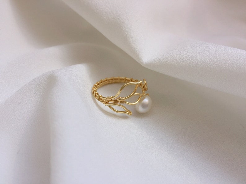 May include: A gold ring featuring a delicate wire design resembling branches, adorned with a single white pearl.